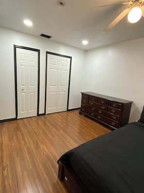 A bedroom with a wooden floor, a bed, a dresser, and two white doors. - Remodeled 4BR Home– 2 FloorsExpansive Retreat 4BR 3.5BA Perfect for Groups (Ocala)