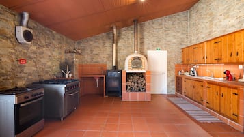A kitchen with a stone wall, a wood stove, a gas stove, and a sink.