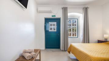 Hotellihuone, jossa on sänky, penkki pyyhkeineen, ovi ja ikkuna.