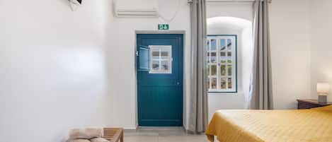 A hotel room with a bed, a bench with towels, a door, and a window.