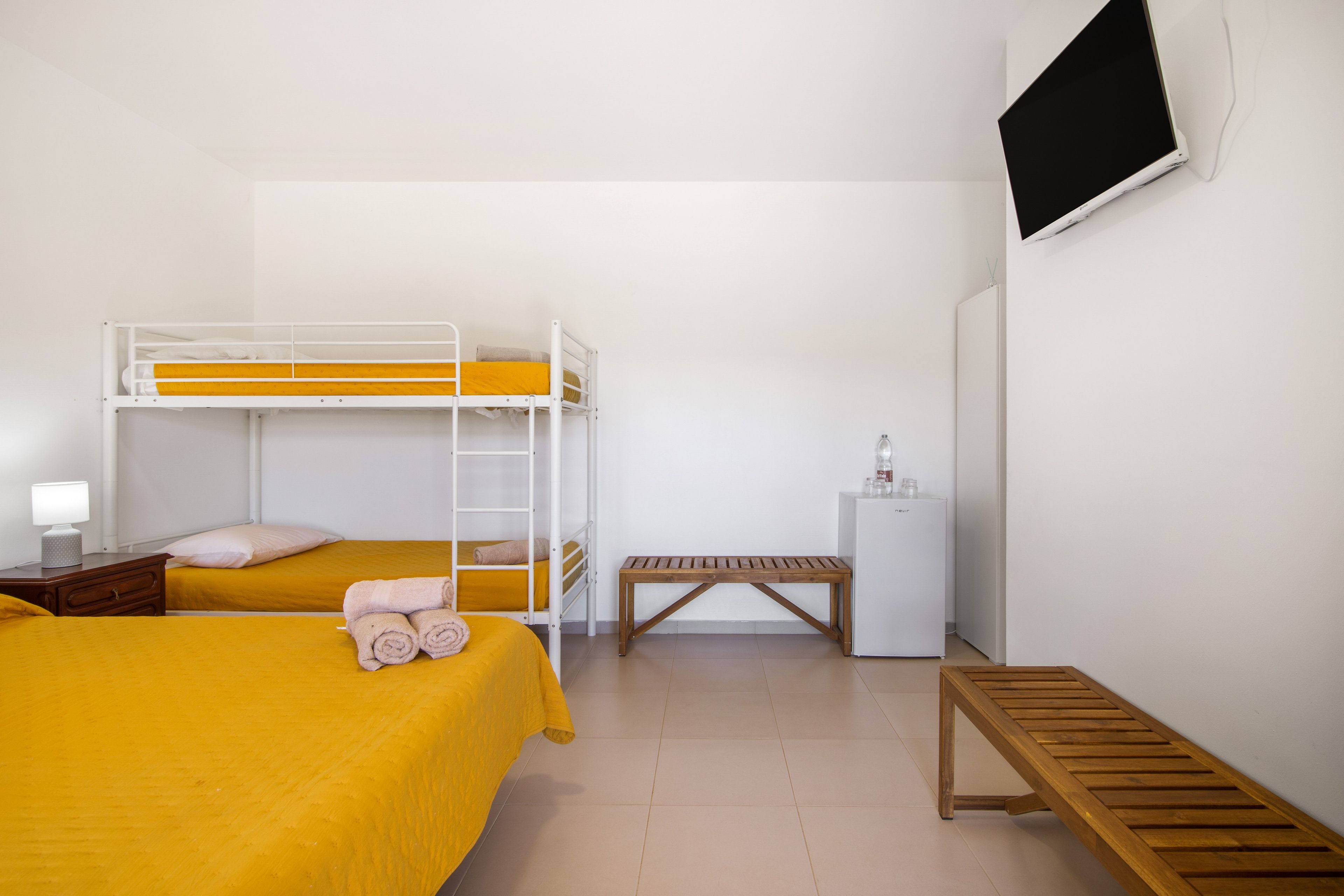 Ein Zimmer mit Etagenbetten, einer hölzernen Bank, einem kleinen Tisch und einem Kühlschrank.