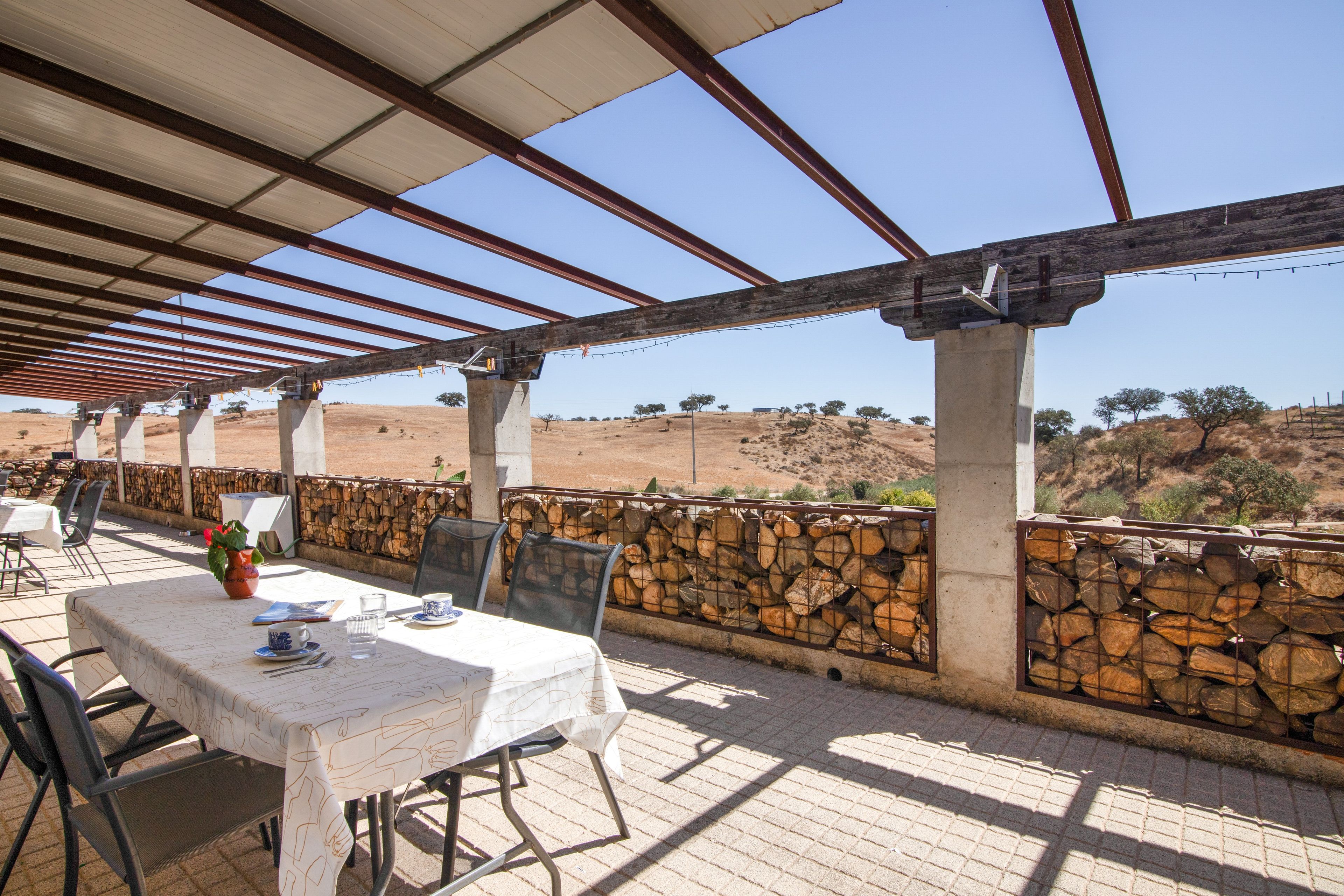 Un patio al aire libre con una mesa lista para comer, un muro de piedra y vistas a un paisaje montañoso.