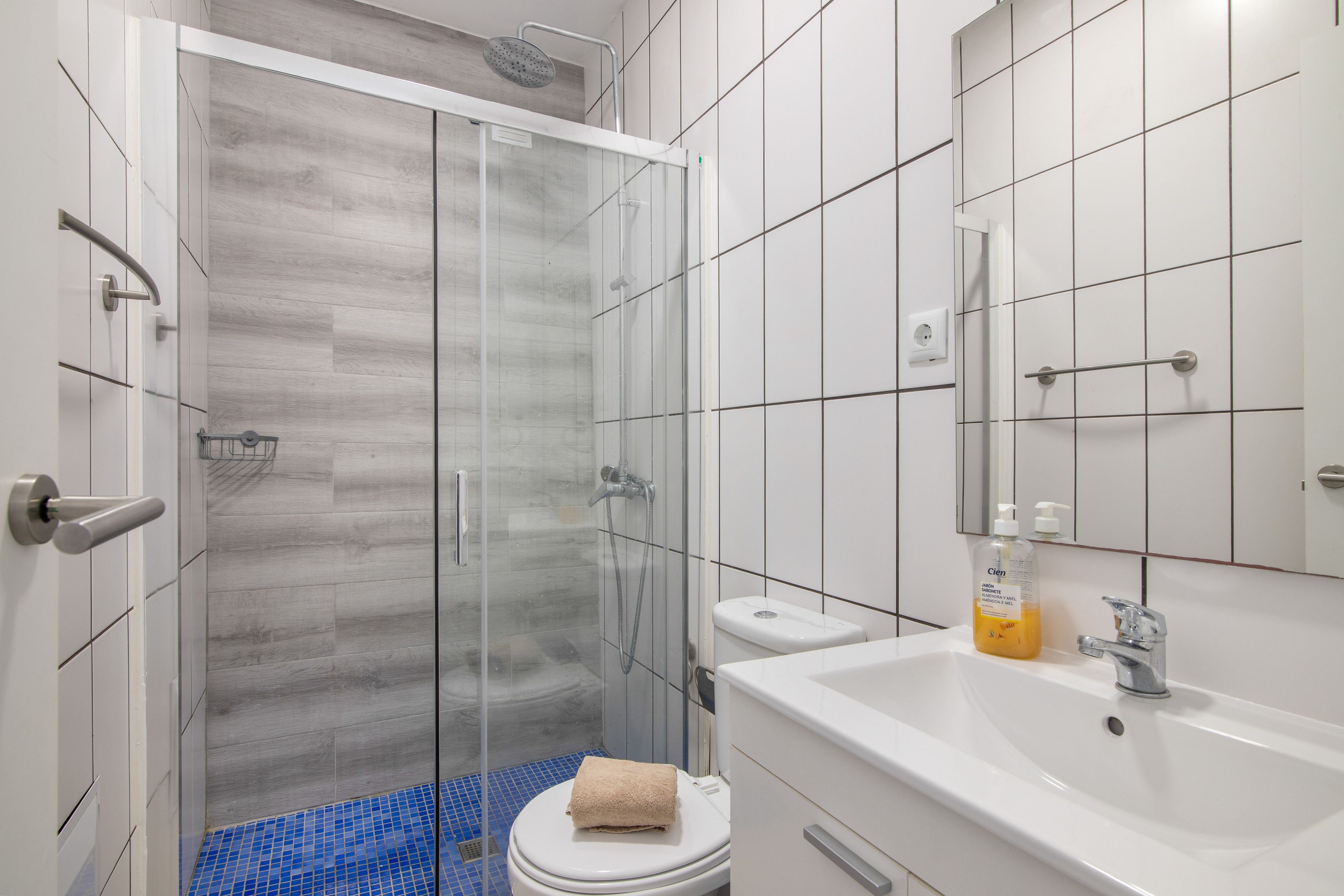 Un baño moderno con cabina de ducha de vidrio, un inodoro blanco, un lavabo con espejo y artículos de aseo.