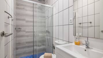 Un baño moderno con cabina de ducha de vidrio, un inodoro blanco, un lavabo con espejo y artículos de aseo.