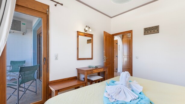 Habitación de hotel con cama, escritorio, silla, espejo y puerta que da a otra habitación.
