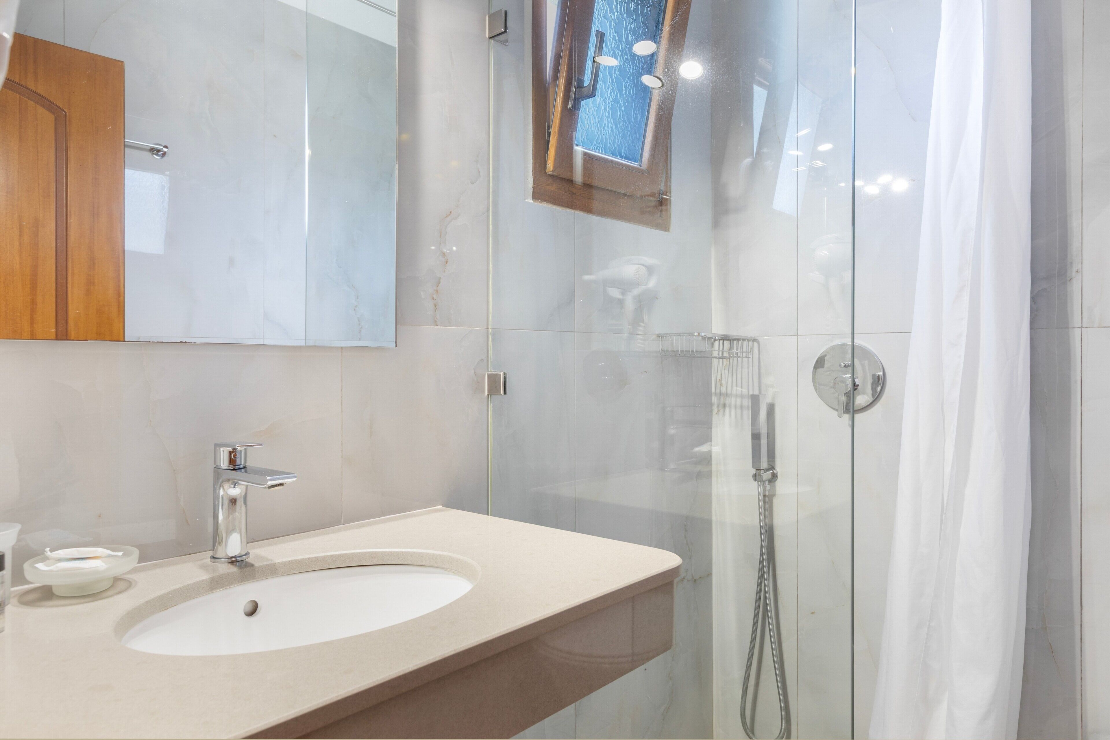 Ein modernes Badezimmer mit einer gläsernen Duschkabine, einem Waschbecken mit Armatur aus Chrom und einem Spiegel über dem Waschbecken.