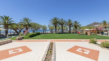 A paved walkway with palm trees and a grassy area, leading to a beach.