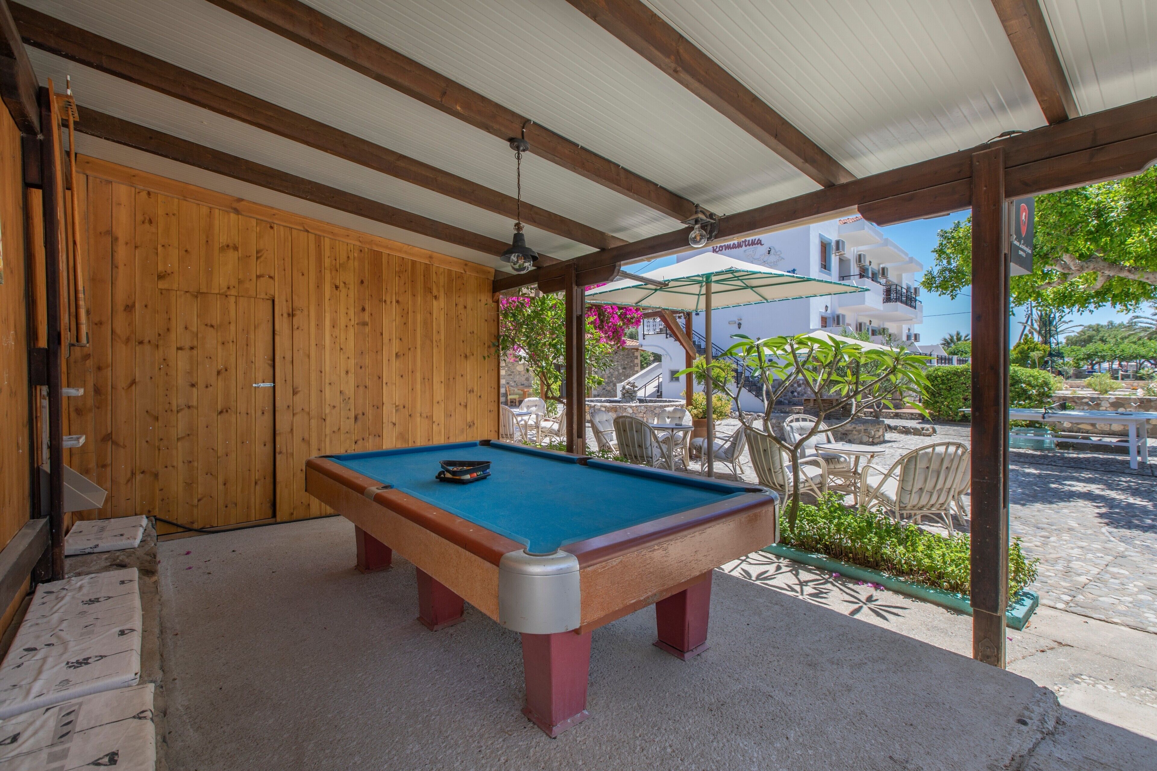 A pool table in a covered outdoor area with a wooden wall and a view of a building with balconies.