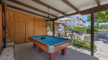 A pool table in a covered outdoor area with a wooden wall and a view of a building with balconies.