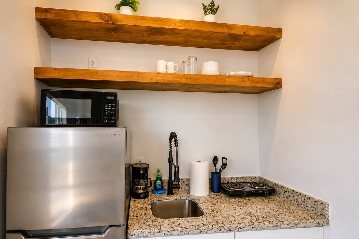 A compact kitchen with a stainless steel refrigerator, a microwave, a coffee maker, and a gas stove.