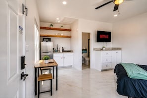 A modern apartment with a kitchen, a dining area, a living room with a bed, and a TV displaying 'NETFLIX'. - #17 | Modern SPI Studio | Beach Walk + Pool | Gulf (South Padre Island)