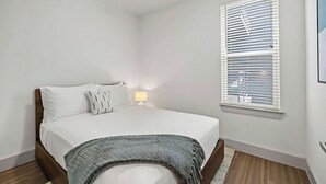 Ein Schlafzimmer mit einem Bett, einem Deckenventilator, einem Fenster mit Jalousien und einer Nachttischlampe.