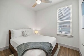 A bedroom with a bed, a ceiling fan, a window with blinds, and a bedside lamp. - Premium Two Bedroom with Balcony & Laundry at Placemakr Downtown Austin (Austin)