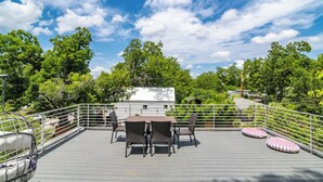 En tagterrasse med et bord og stole, omgivet af et gelænder, med udsigt over et frodigt, grønt landskab.