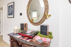 A room with a wooden console table, a framed map, a mirror with decorative elements, and two speakers. - La Holly Rooftop Retreat w/ hot tub (Austin)