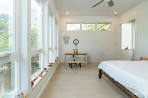 Ein Schlafzimmer mit einem Bett, einem Schreibtisch mit Stuhl, einem Deckenventilator und großen Fenstern.