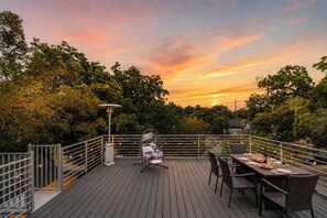 A deck with a dining table and chairs, surrounded by trees and a sunset. - La Holly Rooftop Retreat (Austin)