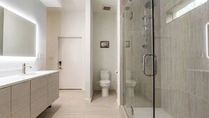 Et moderne badeværelse med en bruseniche med glasvægge, et stort spejl og et toilet.