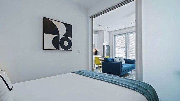 Ein Hotelzimmer mit einem Bett, einem an der Wand hängenden abstrakten Kunstwerk und Blick in den Wohnbereich.
