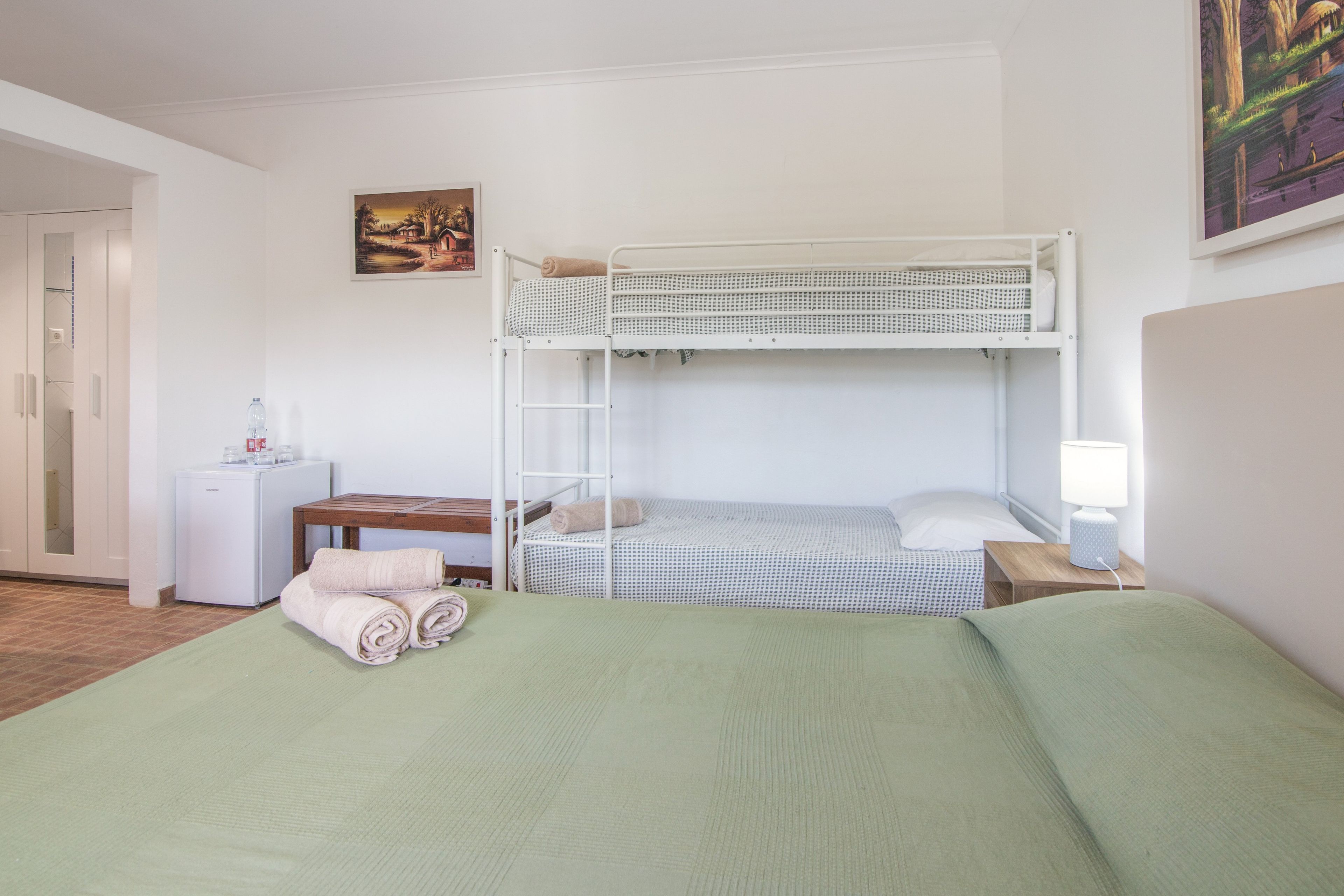 Une chambre avec un lit superposé, un bureau, une lampe et un tableau accroché au mur.