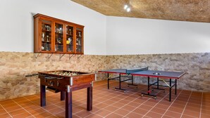Une pièce avec un baby-foot, une table de ping-pong et une vitrine à trophées, le tout adossé à un mur en pierre.