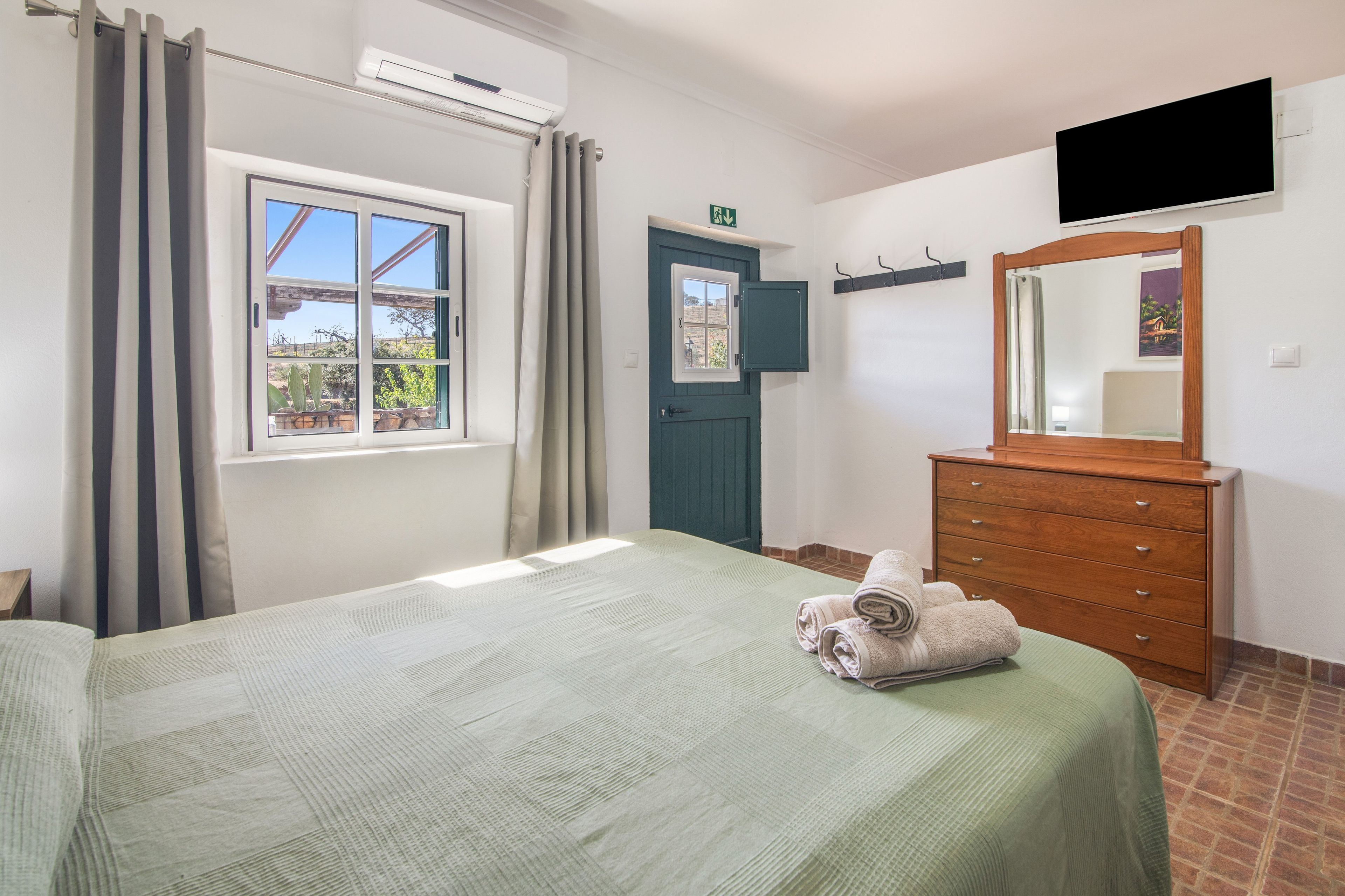 A hotel room with a bed, a dresser, a mirror, and a window with curtains.