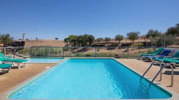 A swimming pool with a clear blue water, surrounded by a fence, and a few lounge chairs.
