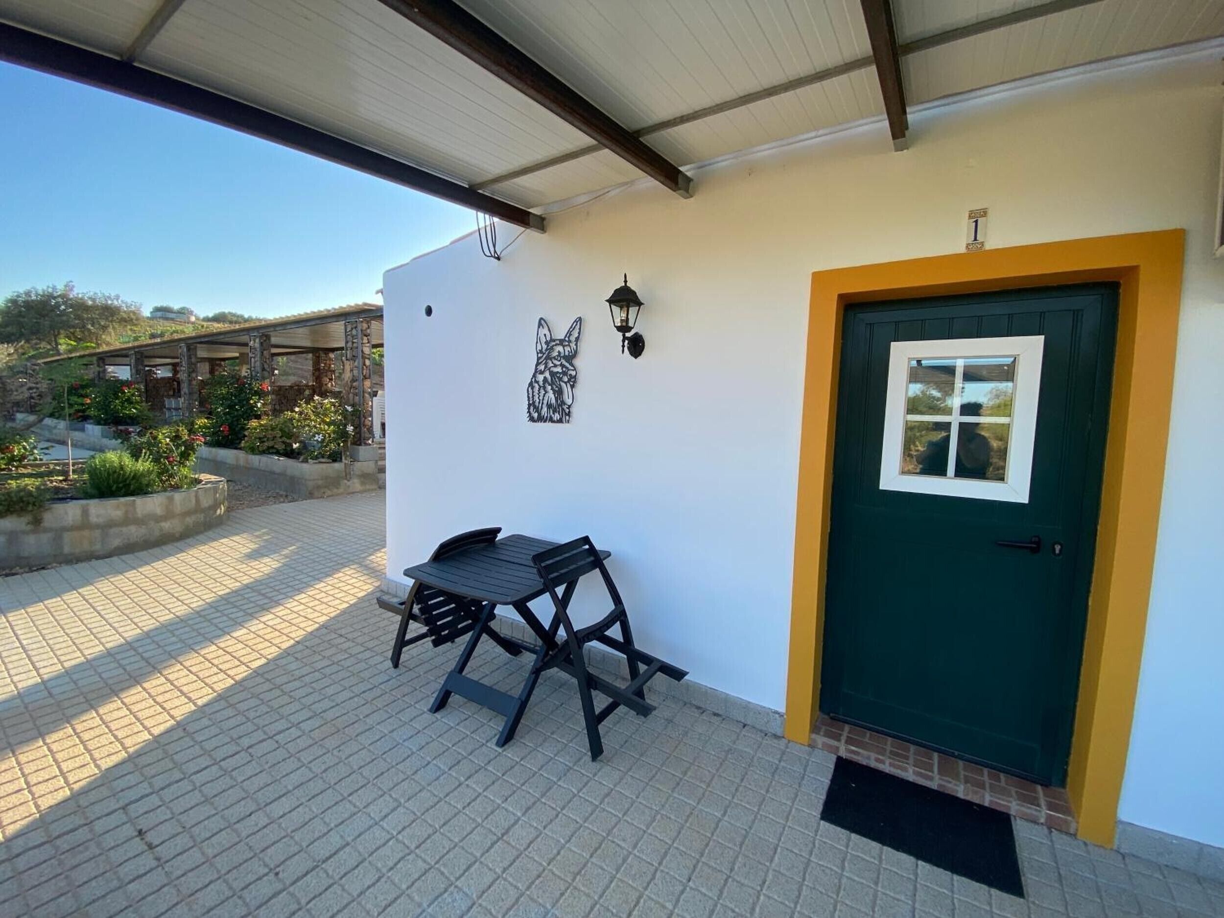 Un patio couvert avec une table et des chaises, une porte verte et un luminaire fixé au mur.