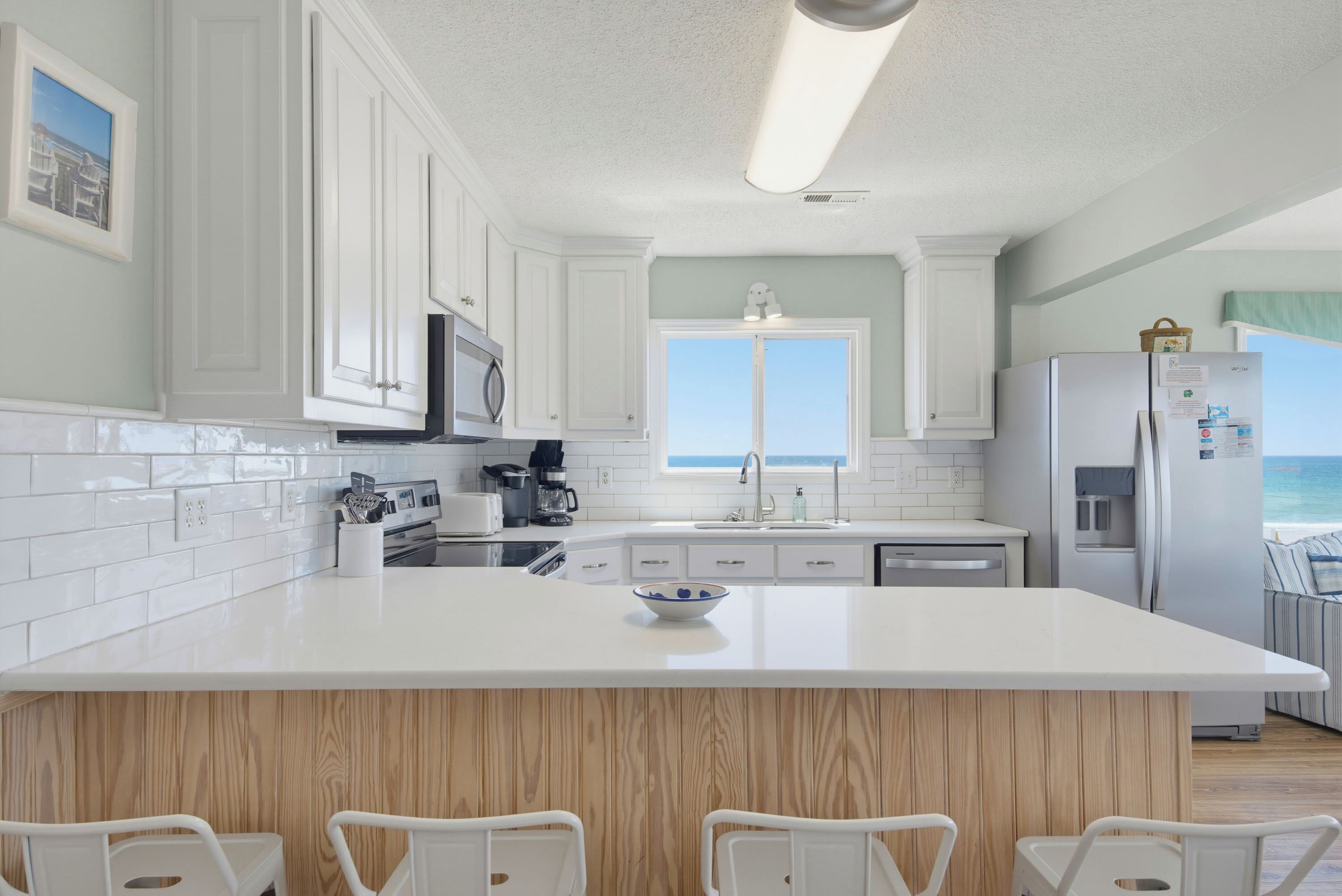 A kitchen with white cabinets, a large island, and a view of the ocean.