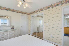A bedroom with a bed, dresser, mirror, and a door leading to another room. - Oceanfront cottage with crow’s nest (North Topsail Beach)