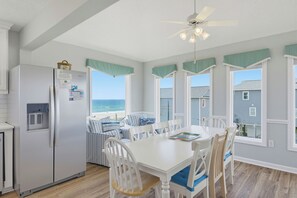 A kitchen with a refrigerator, dining table, chairs, and a view of the ocean. - Oceanfront cottage with crow’s nest (North Topsail Beach)