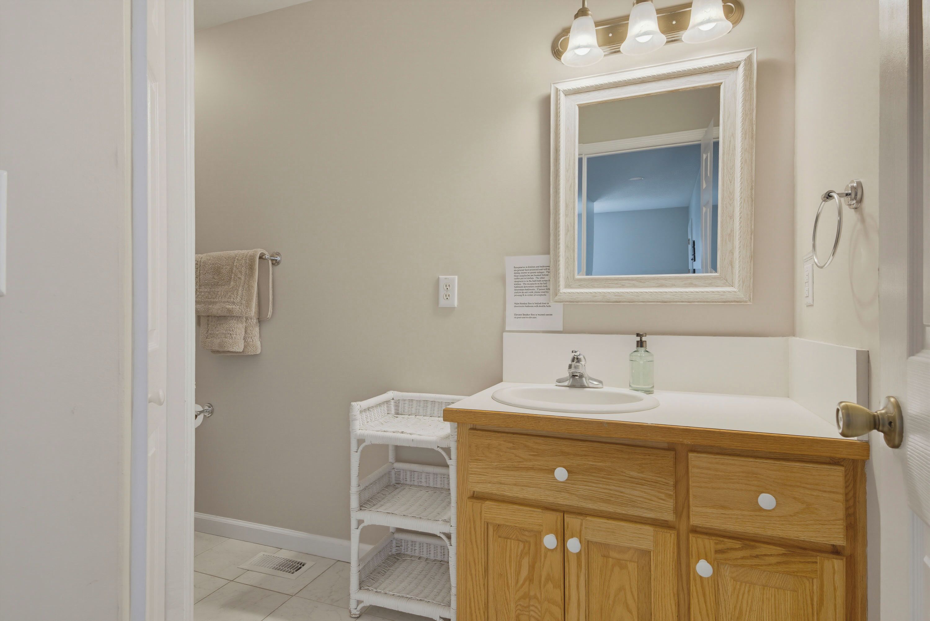 A bathroom with a white sink, wooden vanity, a mirror, a white wicker basket, and a towel hanging on the wall.