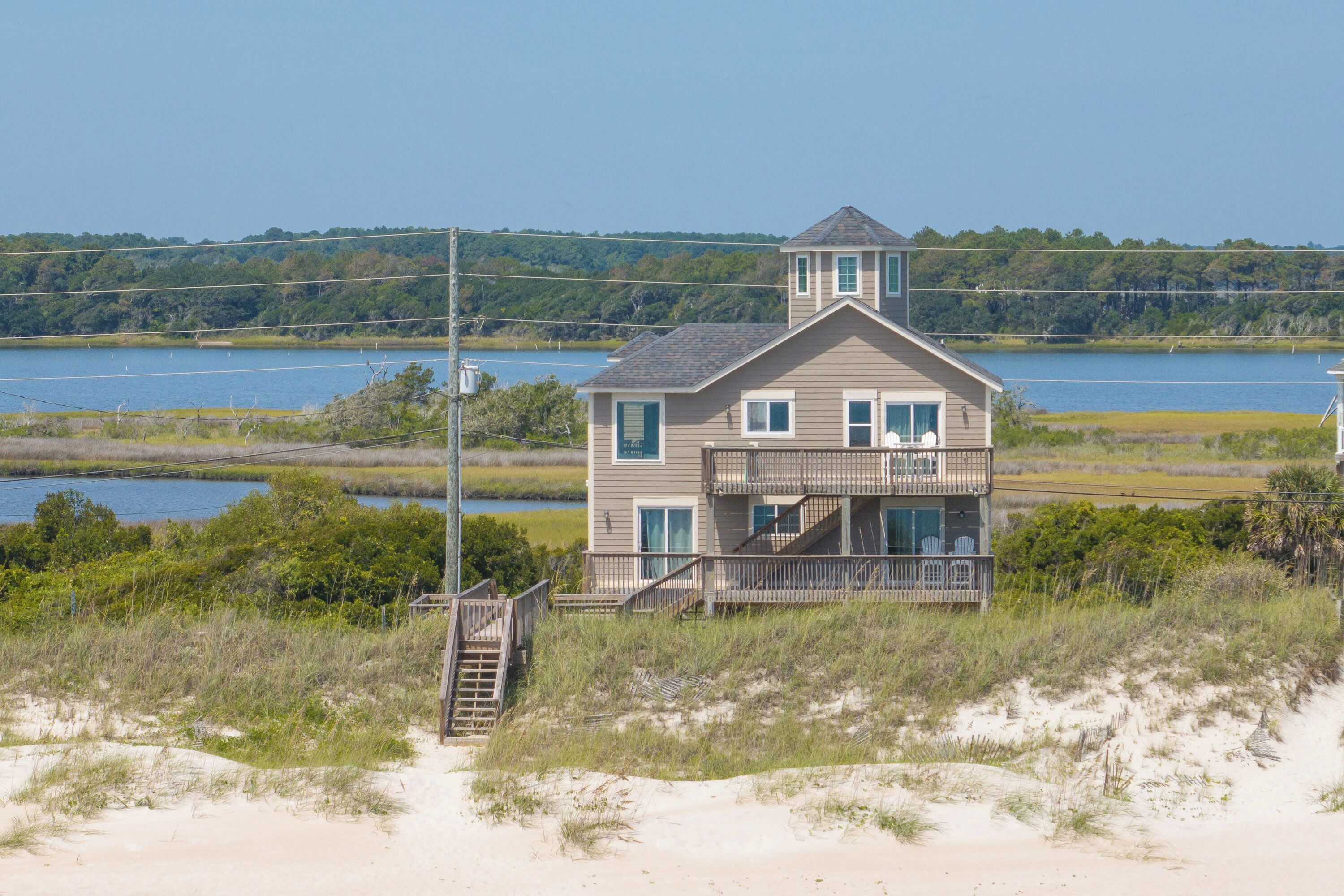 A two-story house with a balcony, located near a body of water and surrounded by vegetation.