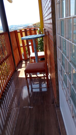 A wooden deck with a table and chair, a brick wall, and a view of the landscape.