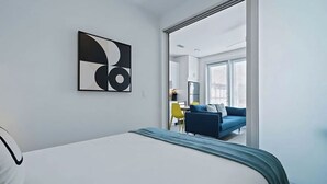 Et hotelværelse med en seng, et abstrakt kunstværk på væggen og udsigt til opholdsstuen.