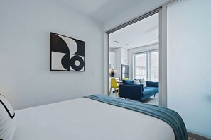 A hotel room with a bed, a wall-mounted abstract artwork, and a view into the living area. - One Bedroom Apartment with Pool access | Near 3rd St Attractions (Austin)