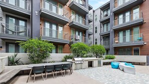 Et moderne lejlighedskompleks med udendørs siddepladser, grill og et mønstret terrassedæk.