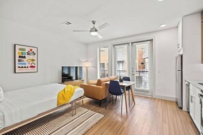 A modern hotel room with a bed, a desk, a chair, a lamp, and a ceiling fan. - Studio Courtyard room at Placemakr Downtown Austin  | Pool access + Amenities (Austin)