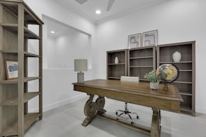 A room with a wooden desk, a chair, a lamp, a globe, and shelves with decorative items. - DOMINICA ISLES 201 | Luxury Retreat at Isles of Collier Preserve (Naples)