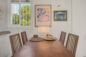 A dining area with a wooden table, six chairs, a lamp, and two framed artworks on the wall. - Panoramic Views Apartment Near Coast & Nature with Sea Views (Vélez-Málaga)