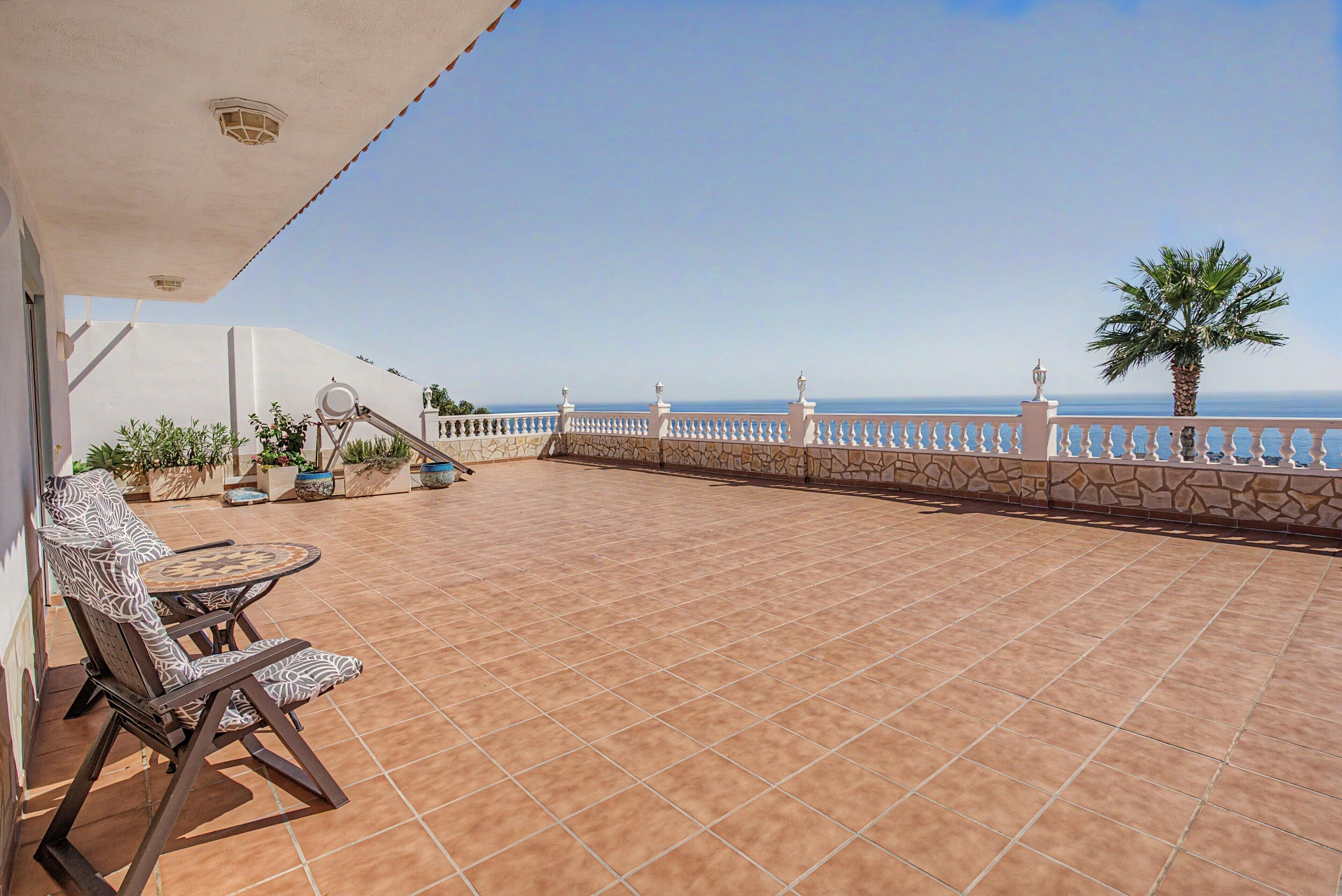 A terrace with a view of the sea, a white railing, and potted plants.
