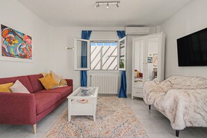 Et moderne soveværelse med en rød sofa, et hvidt sofabord, en blød hvid seng og et stort billede på væggen.
