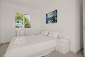 A bedroom with a bed, a nightstand, a bedside lamp, a window, and a painting on the wall. - Panoramic Views Apartment Near Coast & Nature with Sea Views (Vélez-Málaga)