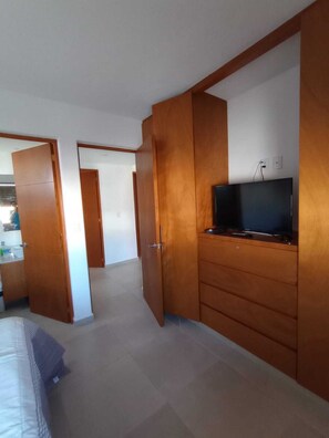Ein Zimmer mit einem Bett, einem Fernseher auf einer Holzkommode und einem durch eine offene Tür einsehbaren Badezimmer.