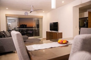 Ein modernes Wohnzimmer mit Glastür zum Balkon, einem Flachbildfernseher und einer Obstschale auf dem Couchtisch.