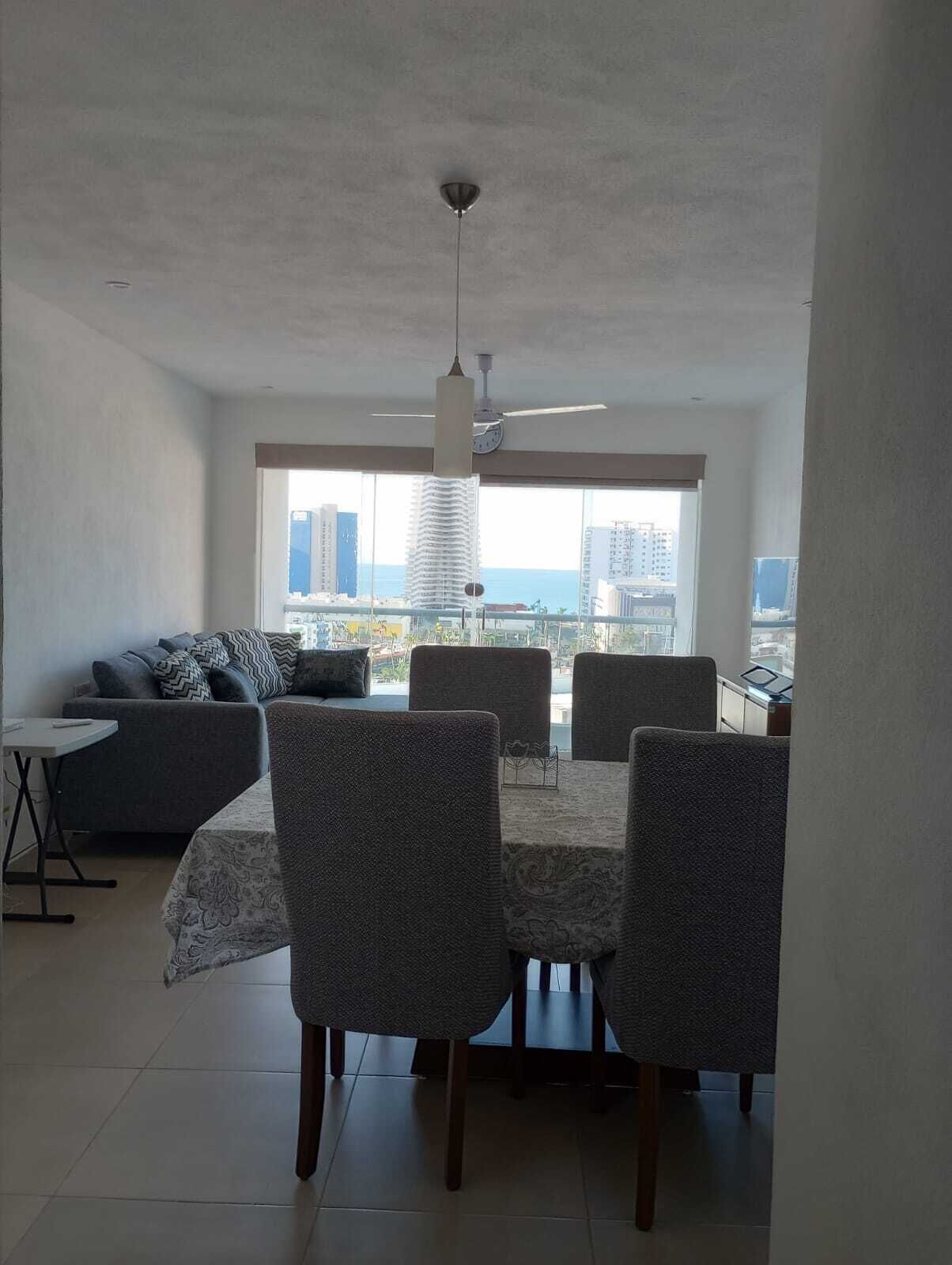 A dining area with a table and chairs, a sofa, and a view of the cityscape through large windows.