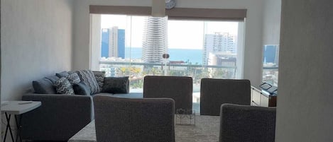 Un espace repas comprenant une table et des chaises, un canapé et une vue sur le paysage urbain grâce à de grandes fenêtres.
