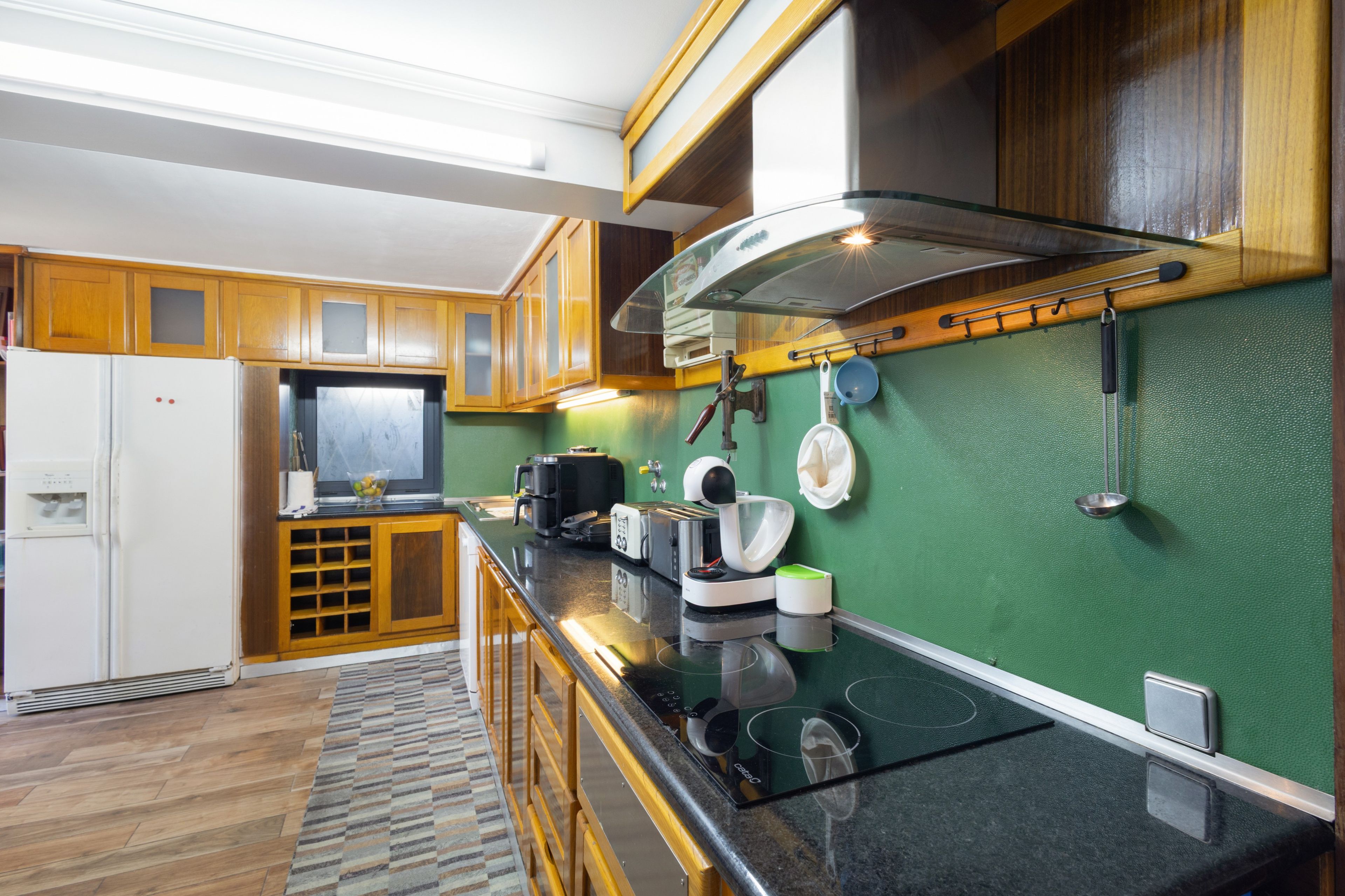 A modern kitchen with wooden cabinets, a built-in oven, and a green wall.