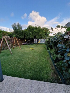 Een achtertuin met een schommel, een kleine boom en een bloembed.