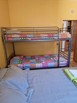 Een stapelbed met kleurrijk beddengoed en een enkel bed met een grijze deken.